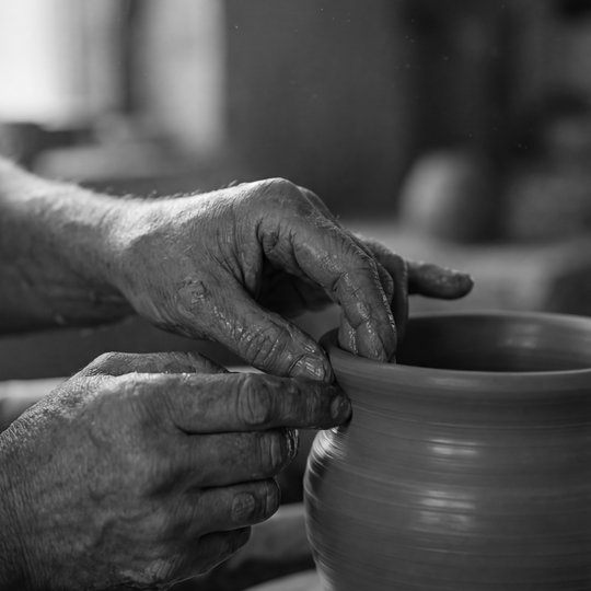 Weathered hands shaping clay on a potter's wheel, warm side light