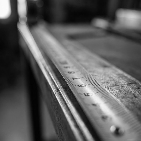 A steel measuring tape pulled taut along a straight metal edge, sharp focus on millimetre markings